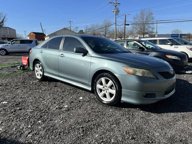 A silver sedan parked on a gravel lot surrounded by other cars, with power lines and trees in the background.