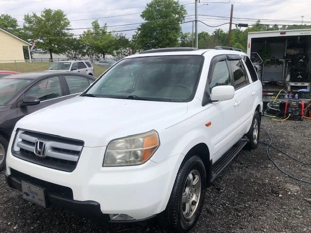 White Honda Pilot parked in a lot with vehicles and equipment nearby.