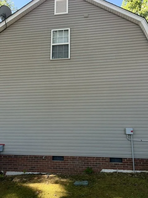 The side of a house with beige vinyl siding, a single window, a small vent at the roof peak, and an electric meter box on the wall.