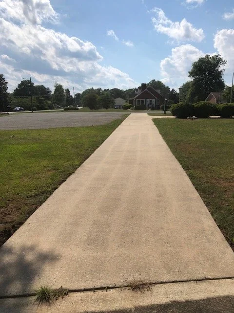A sidewalk leading to houses in a suburban neighborhood on a sunny day with a partly cloudy sky.
