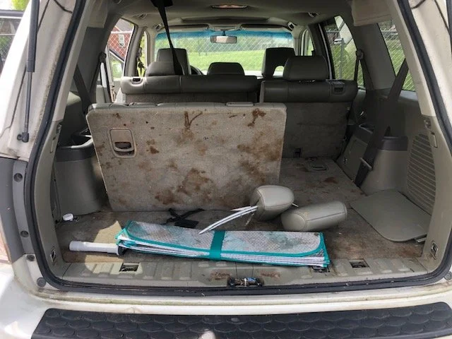 The interior of an SUV with the rear hatch open, showing a dirty and stained cargo area with a folded rug and some tools on the floor.