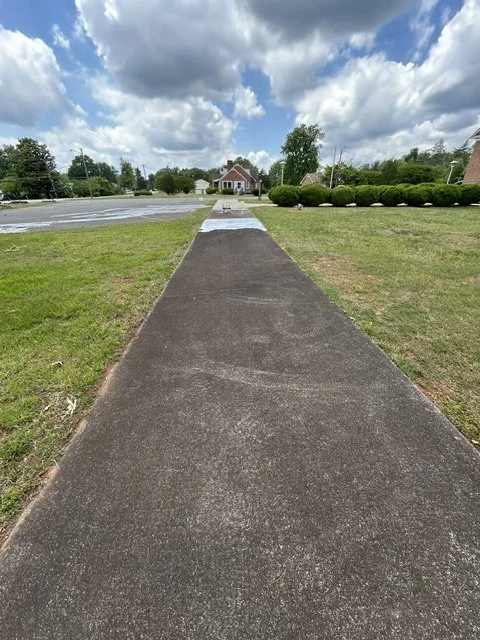 A concrete sidewalk extending toward a residential house under partly cloudy skies in a suburban neighborhood.
