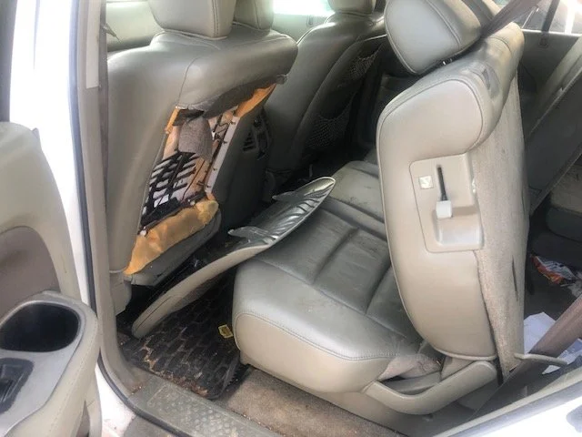 The back seat of a vehicle with the front passenger seat folded forward, exposing the seat frame and motor mechanism beneath it.