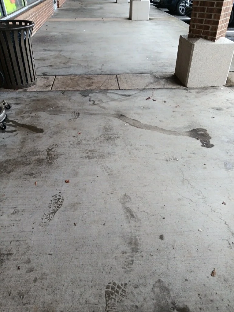 Footprints and shoe marks on a concrete sidewalk outside a building with brick pillars and a garbage can to the side.