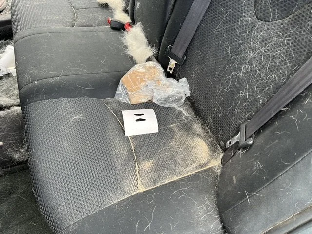 Car backseat with fuzzy debris, a plastic bag with bread, and a white evidence marker with two black bars.