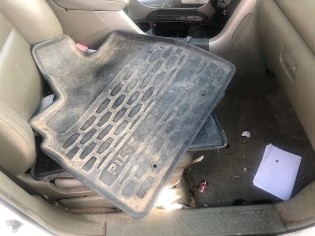 The back seat of a vehicle with a dirty rubber car mat placed on it and a white paper on the floor.