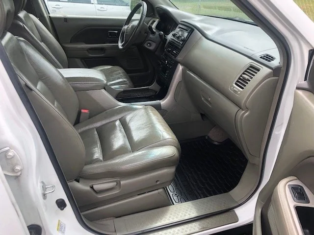 Interior of a vehicle showing the front passenger and driver seats, dashboard, steering wheel, and center console with black rubber floor mats.