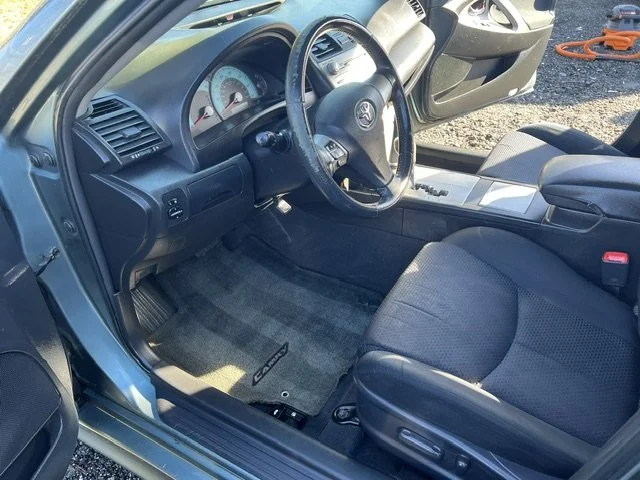 Interior of a car showing the driver's seat, steering wheel, dashboard, and part of the front passenger seat with a new-looking carpeted floor mat.