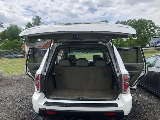 White SUV with open trunk and rear passenger doors, parked outdoors on a gravel area under a cloudy sky.