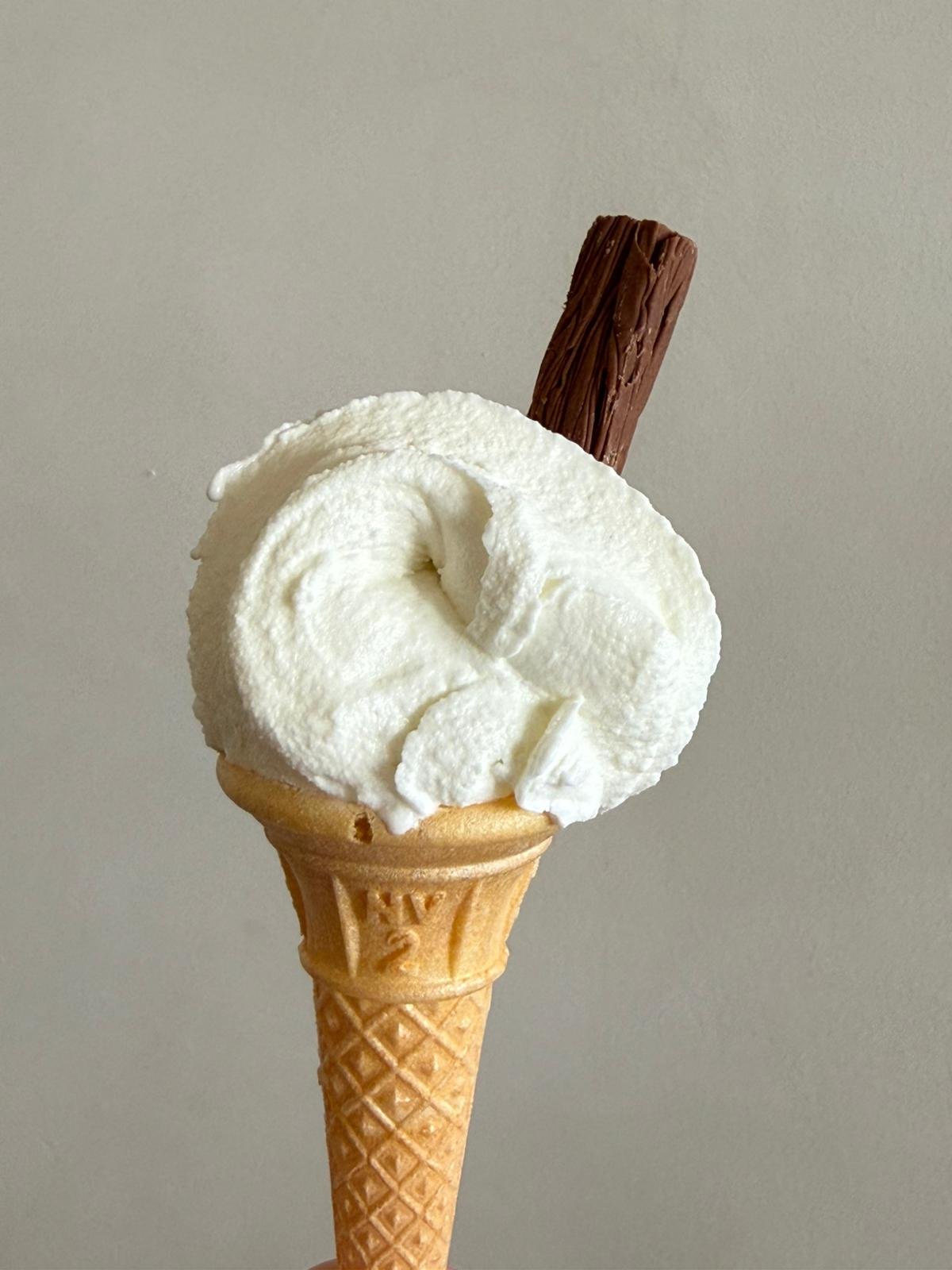 A vanilla ice cream cone topped with whipped cream, with a chocolate stick inserted into the ice cream.
