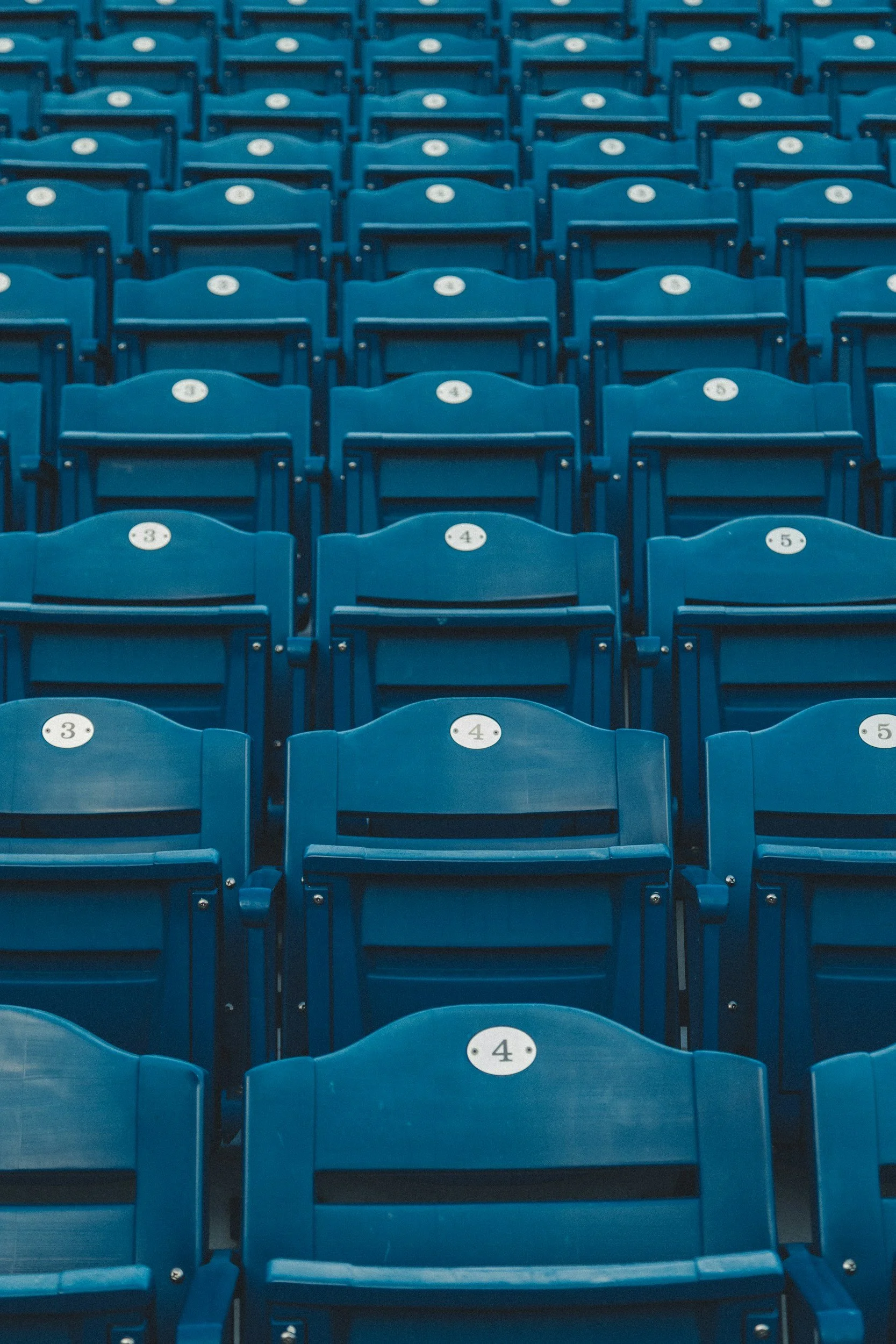 Multiple rows of blue stadium seats, each labeled with a white numbered circular sticker, arranged in a pattern.