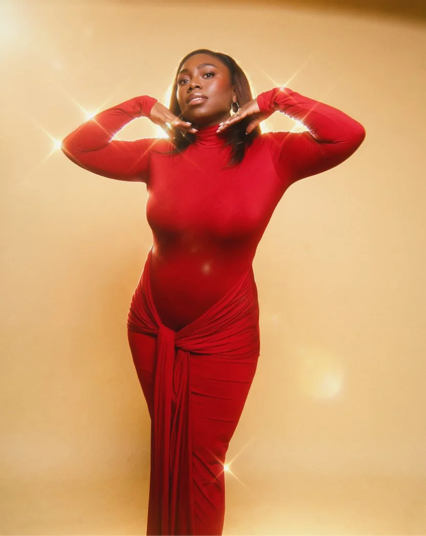 A woman wearing a tight red dress with long sleeves and a high neckline, standing against a beige background with sparkles.