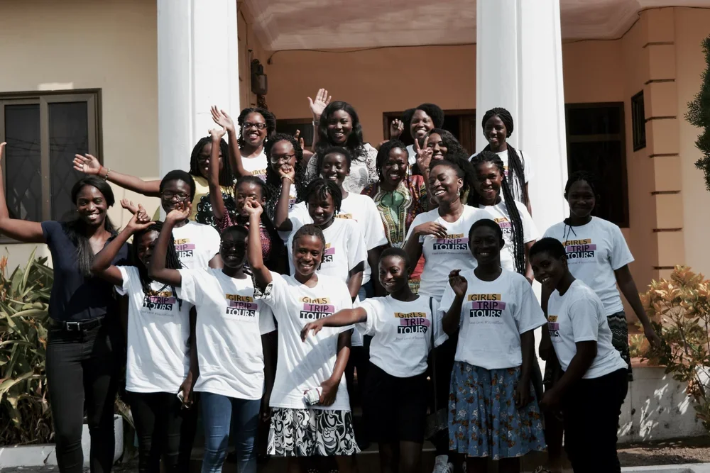Group of smiling girls and women posing on the steps of a building, some wearing shirts that say 'Girls Trip Tours.'