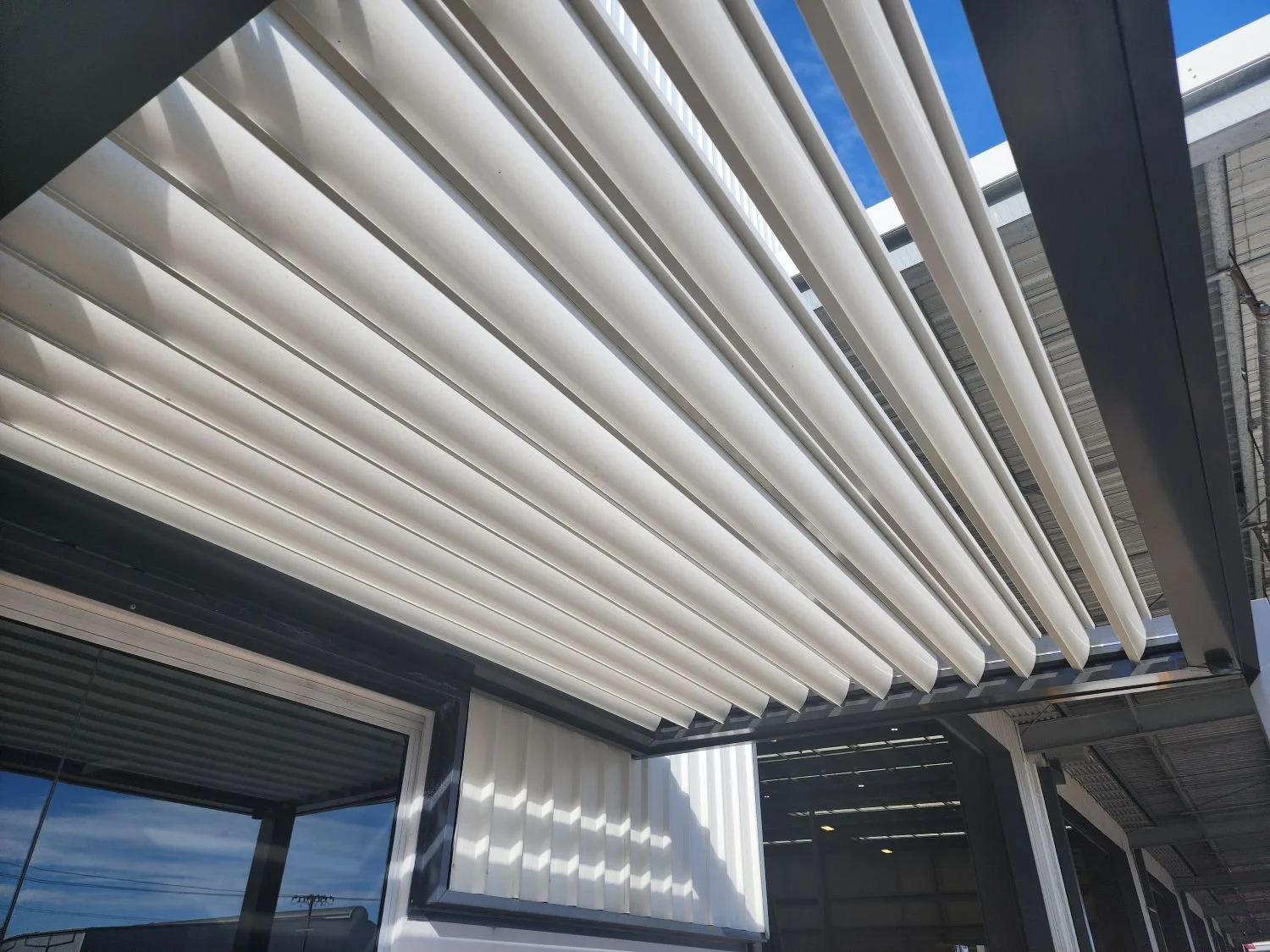 Close-up of a white exterior porch cover with horizontal slats, part of a modern building with a window and roofing structure, under a clear blue sky.