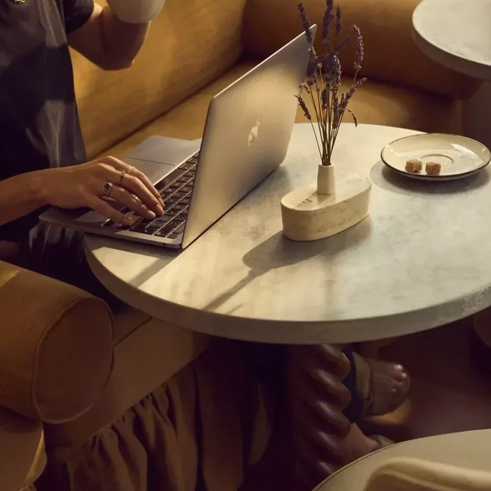 Person working on a laptop at a marble table with a vase of purple flowers and a plate with sugar cubes.