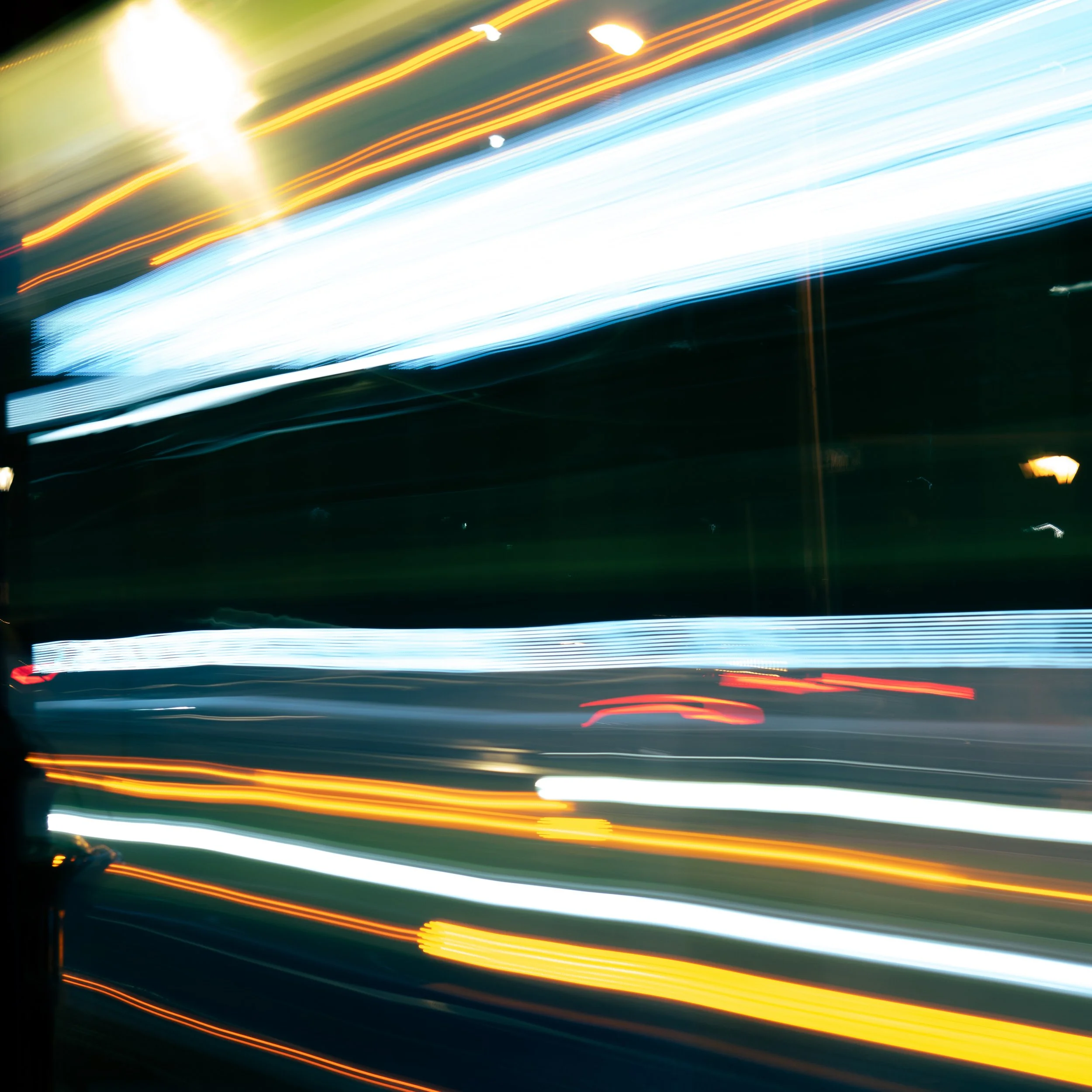 Light trails created by moving lights at night, with streaks of white, blue, and orange across the image.