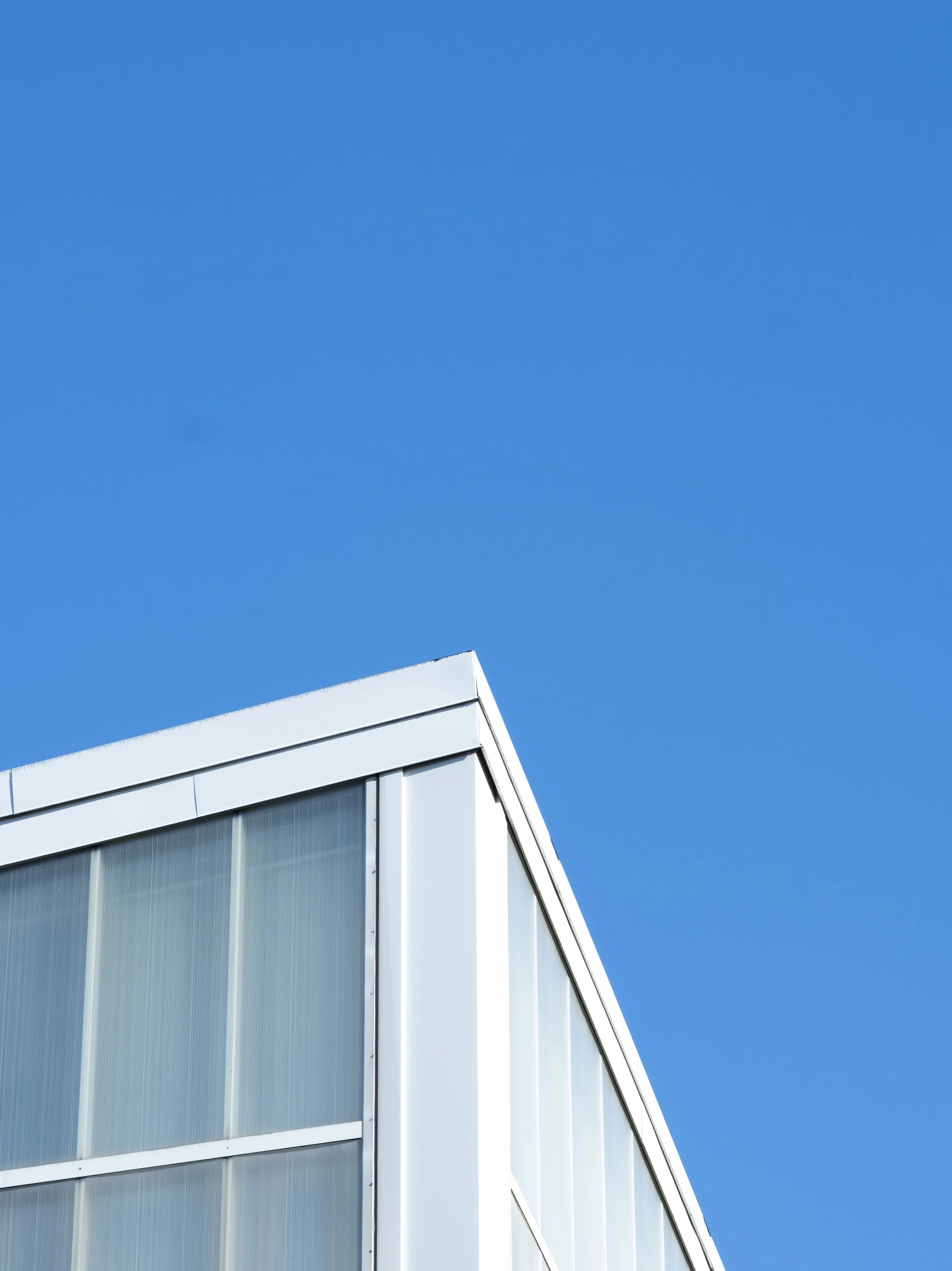 A modern white building with large glass windows seen against a clear blue sky.