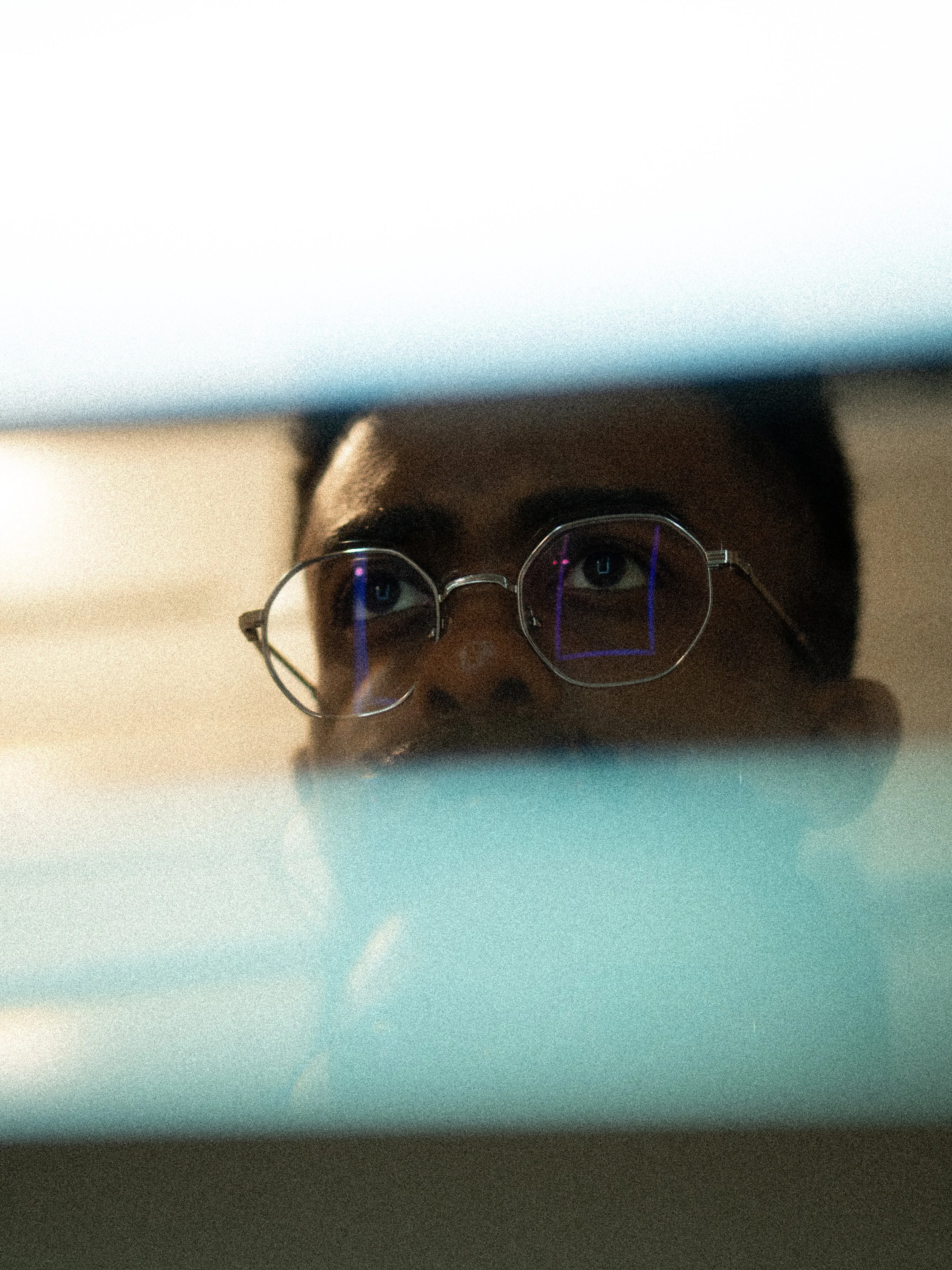 Photo of a person wearing glasses, looking up, with the focus on their face surrounded by a blurred background.