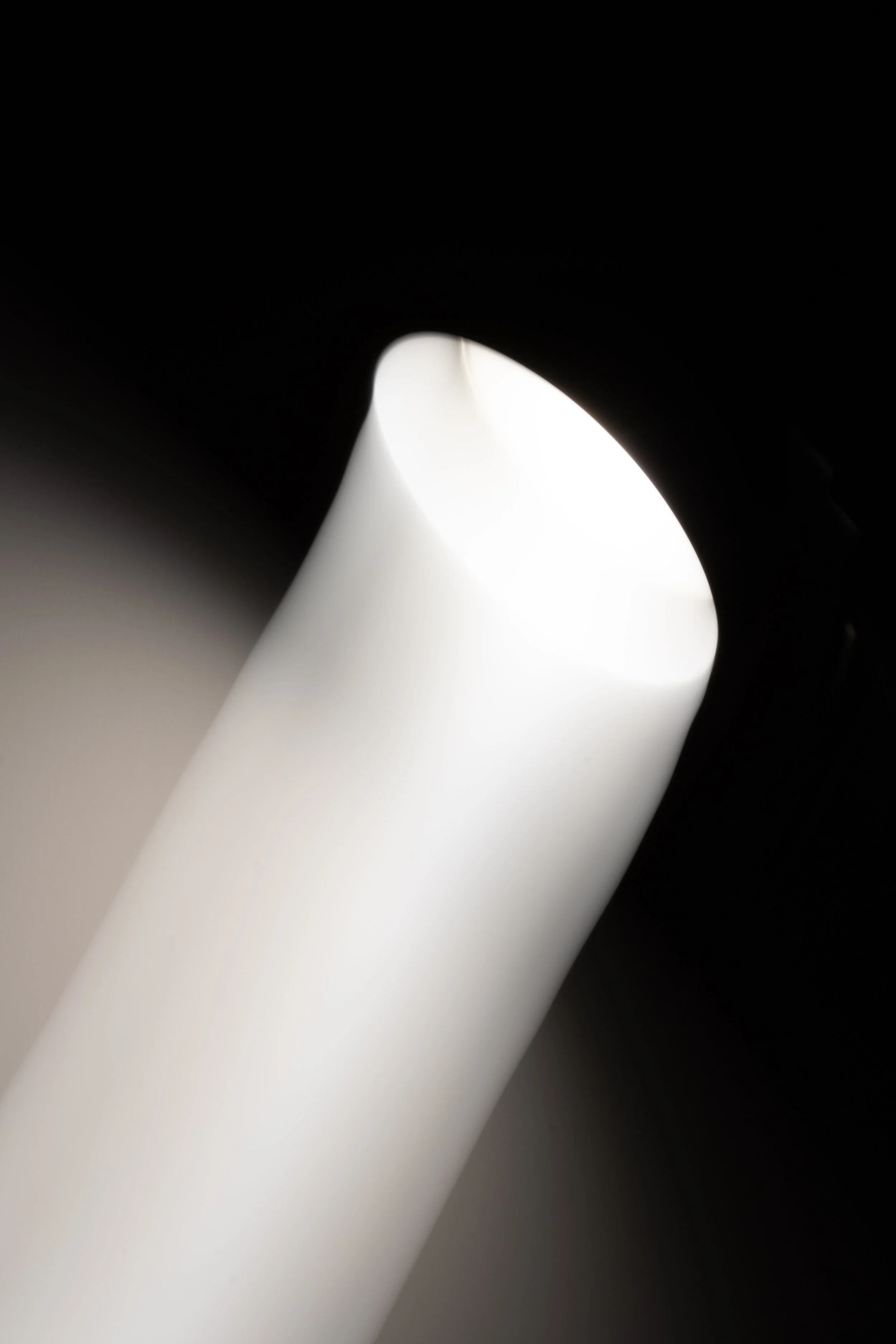 Close-up of a white object with a smooth surface, partially enclosed by a dark, shadowed area, with light illuminating the center area.