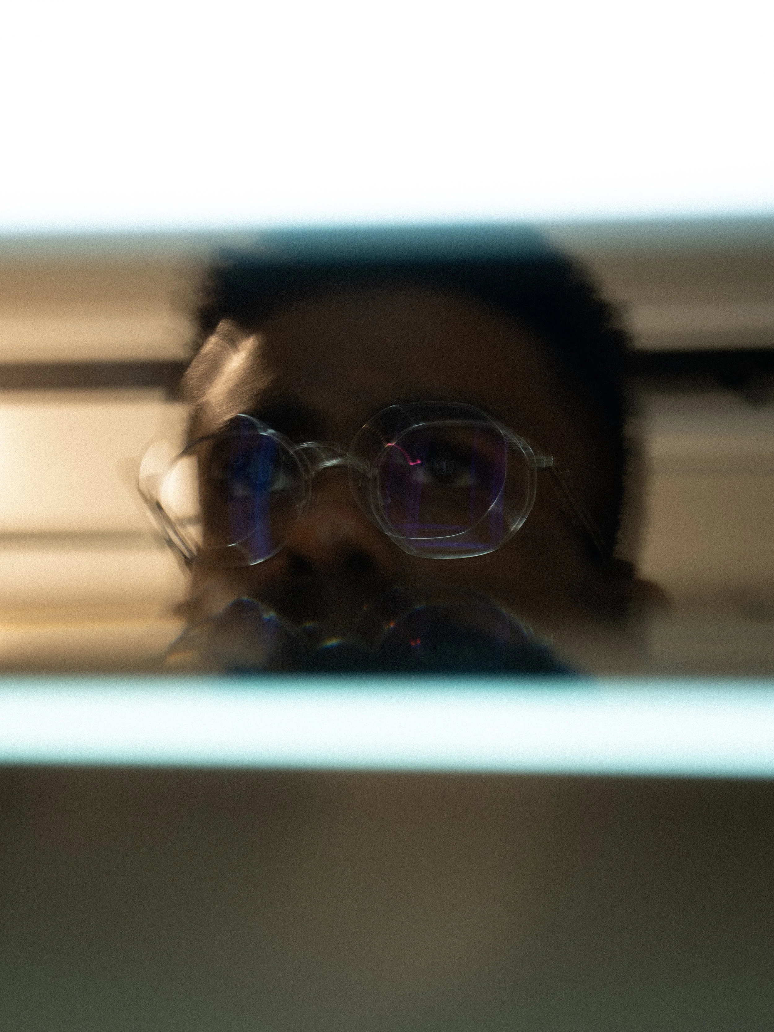 Blurred image showing a person with glasses and short hair, taking a selfie in a mirror, with a blue streak at the top of the image.