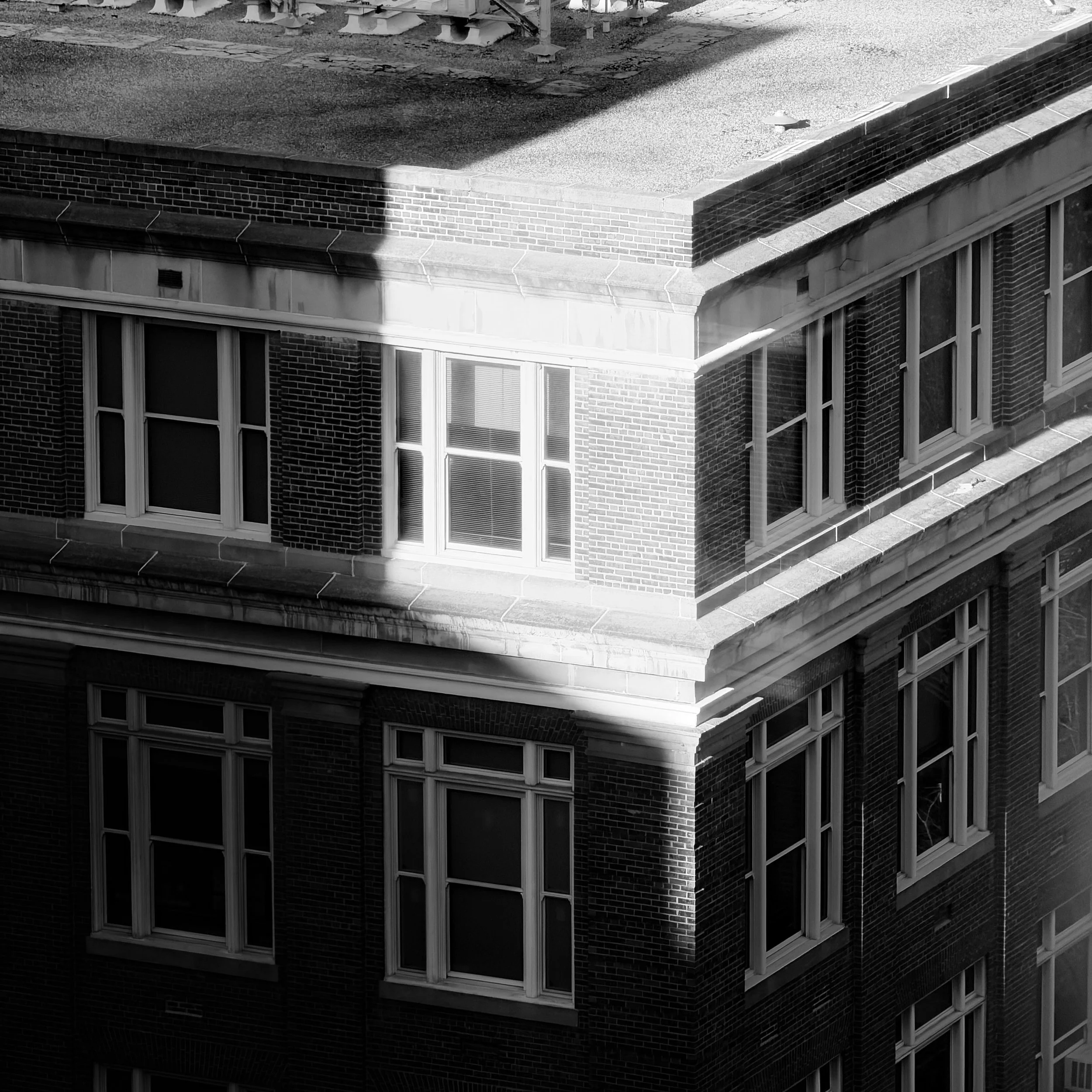 Black and white photo of a brick building with multiple windows and a roof with a parapet wall.