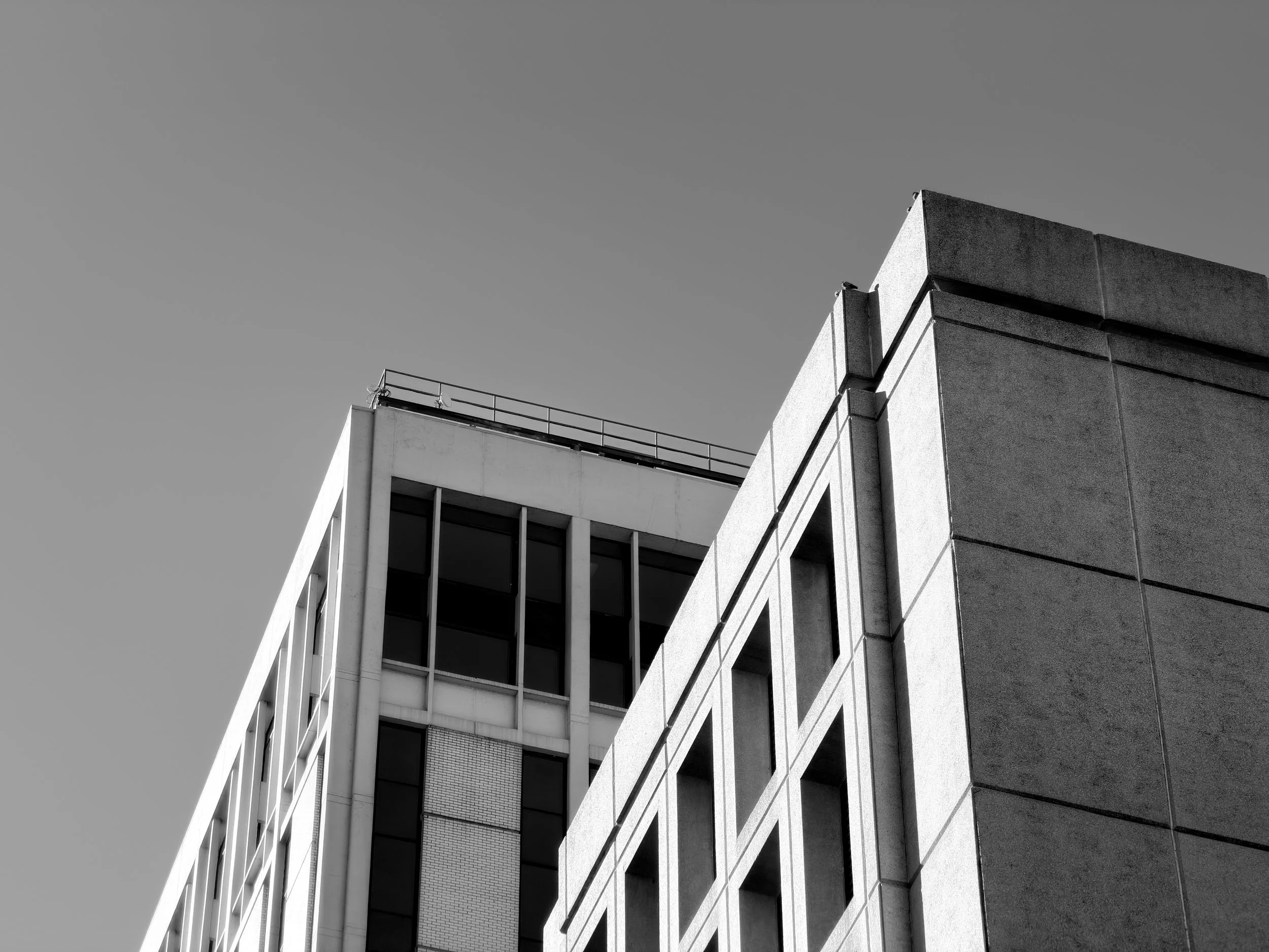 Black and white photo of a modern building with multiple tiers and large glass windows, showing sharp angles and clean lines, against a clear sky.