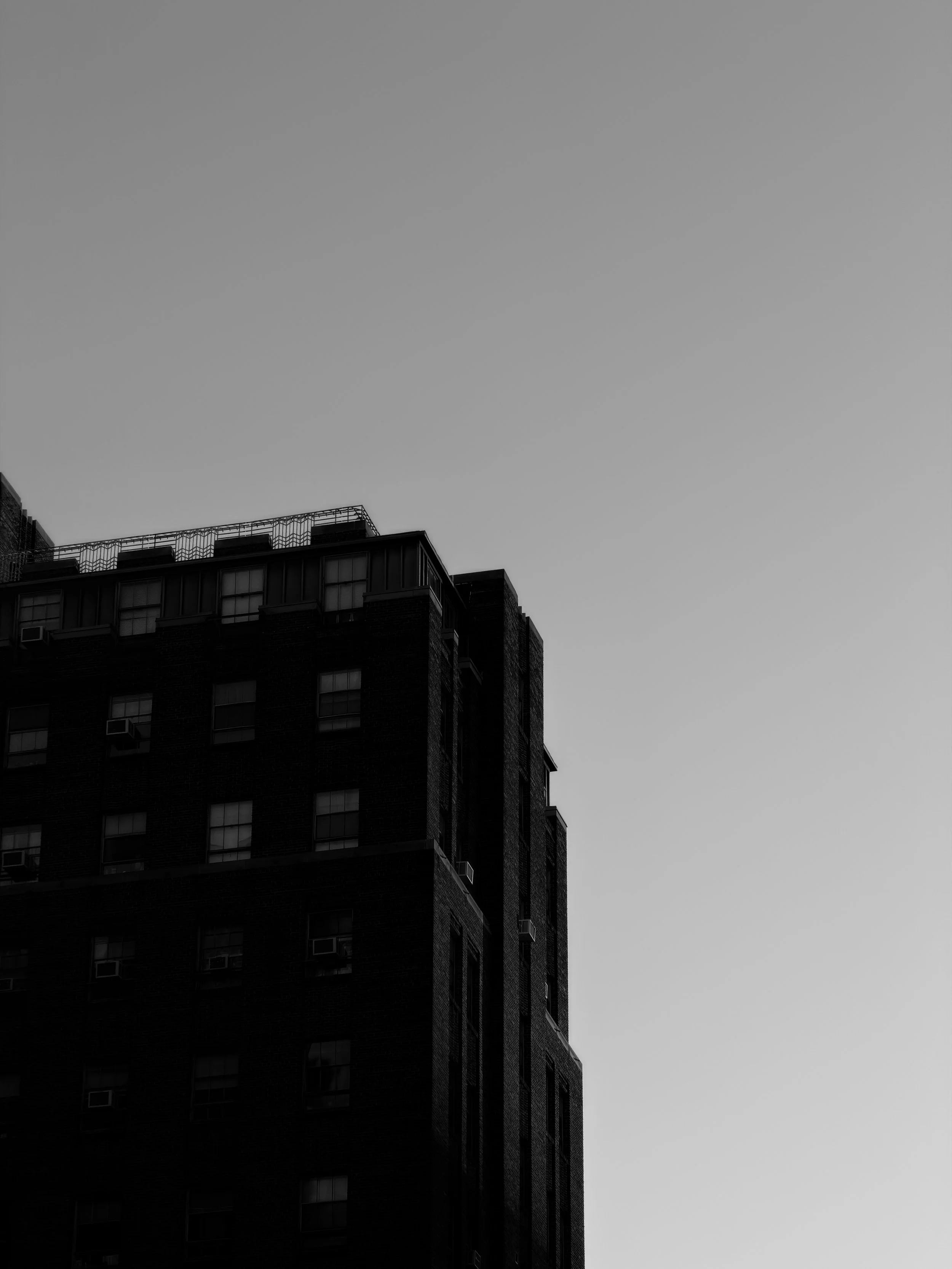 A tall building with multiple windows and a rooftop structure against a plain sky.