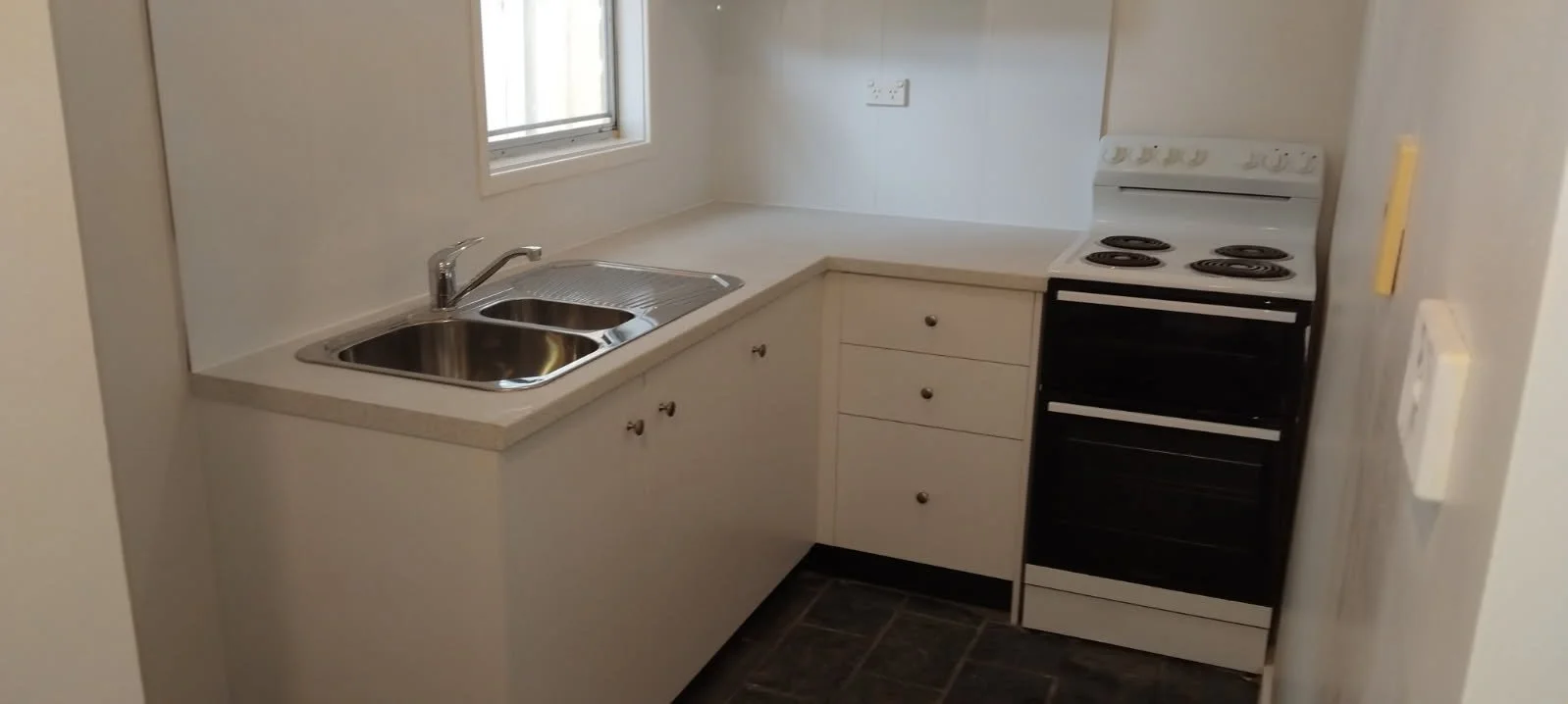Small kitchen with a stainless steel sink, white cabinets, a window, an electric stove, and a white countertop.