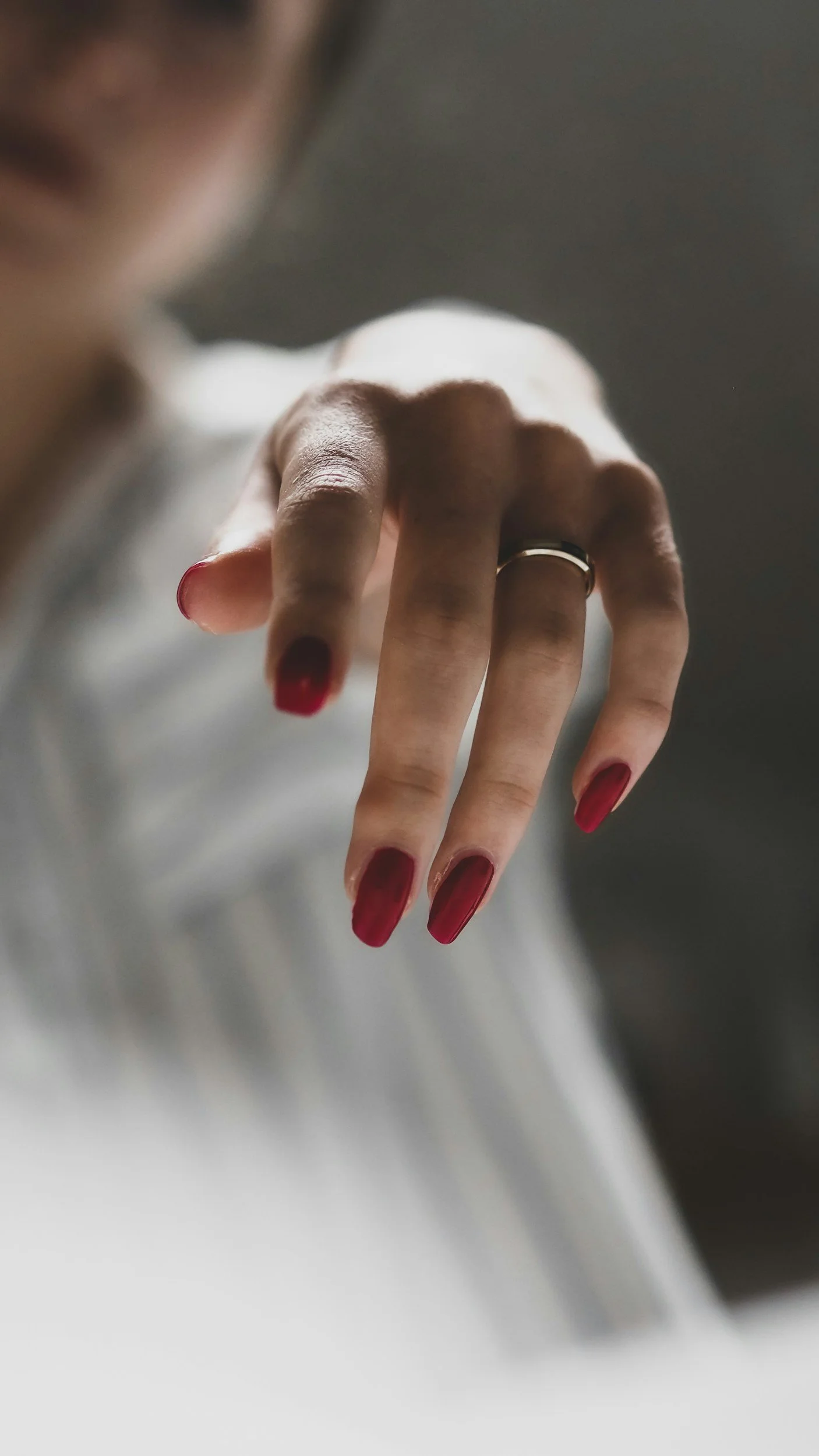 Close-up of a hand with painted red nails and a silver ring, with a blurred person in the background.