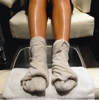 Pedicure picture. Person sitting on a pedicure chair with legs extended, wearing hot steamed towels during a treatment.