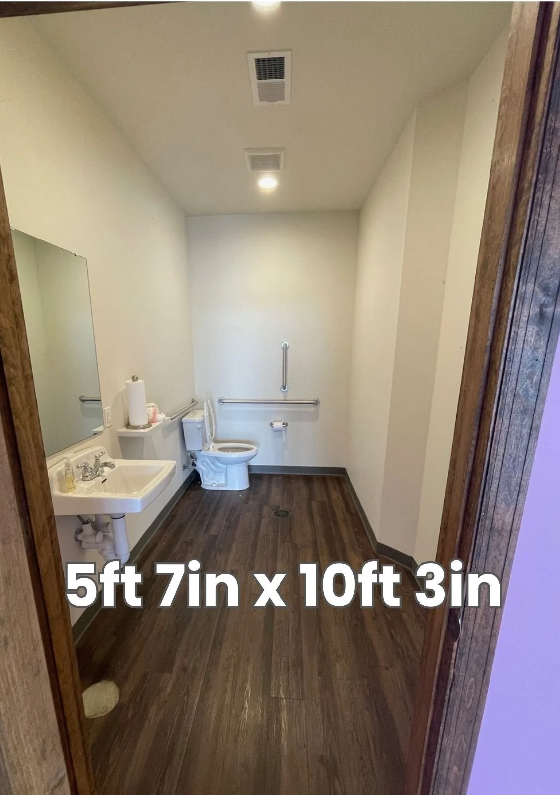 An accessible restroom with a toilet, sink, mirror, and grab bars, measuring 5 feet 7 inches by 10 feet 3 inches.