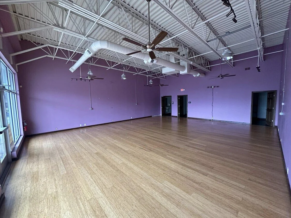Empty room with purple walls, hardwood floor, large windows, ceiling fans, and exposed ductwork.