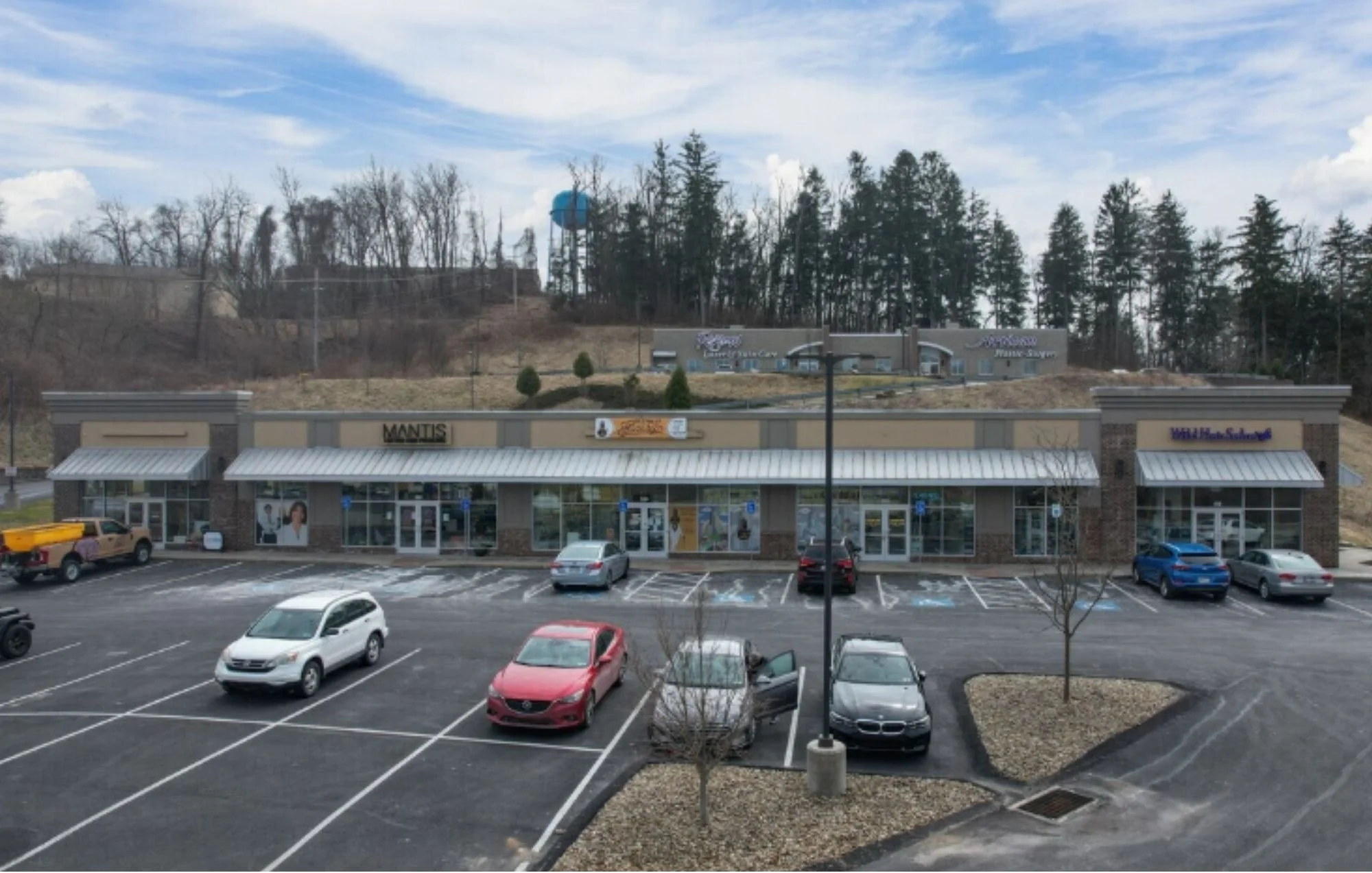A shopping plaza with two large buildings with large parking lot. 4 Storefronts in the lower building and 2 in the upper building.