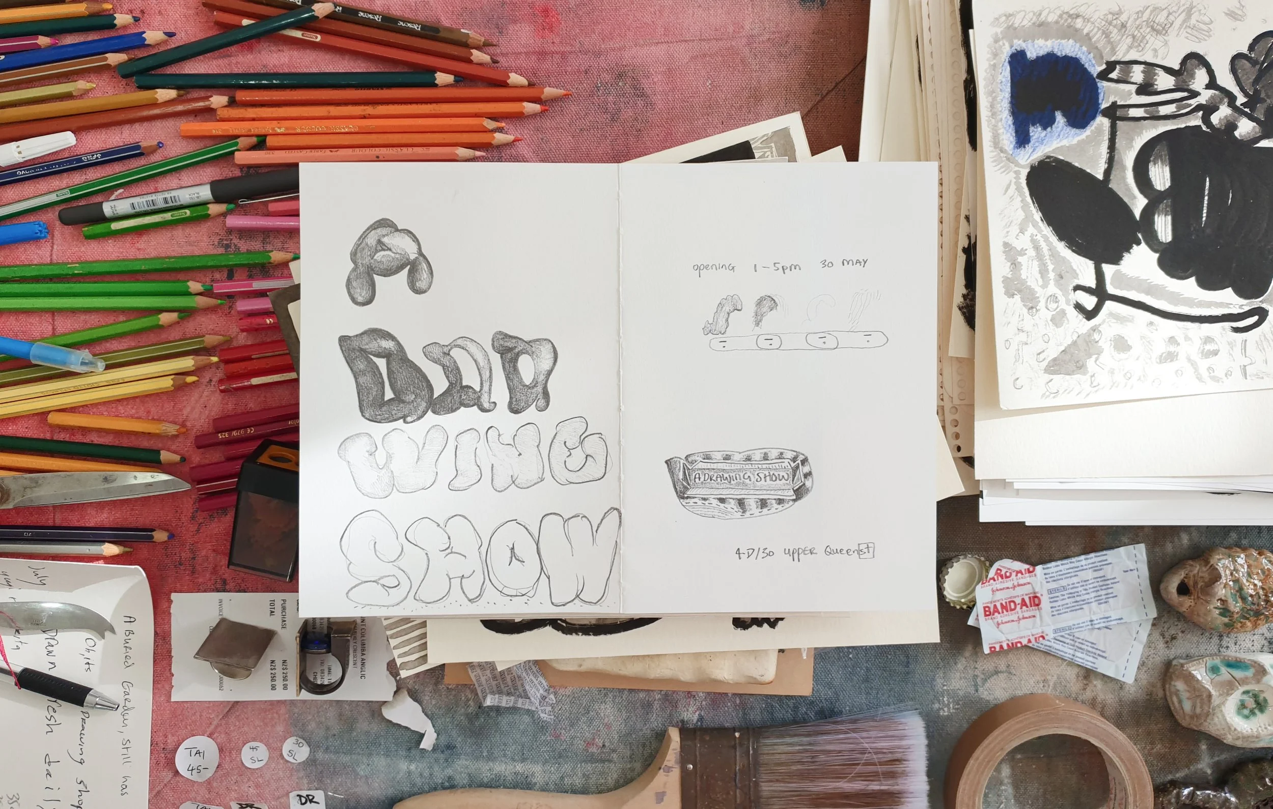 Various art supplies on a pink surface, including colored pencils, pens, and markers. There are sketches and drawings, including one with the phrase 'BAD VIBES' in stylized letters. Some handwritten notes and appointment details are also visible among the supplies.