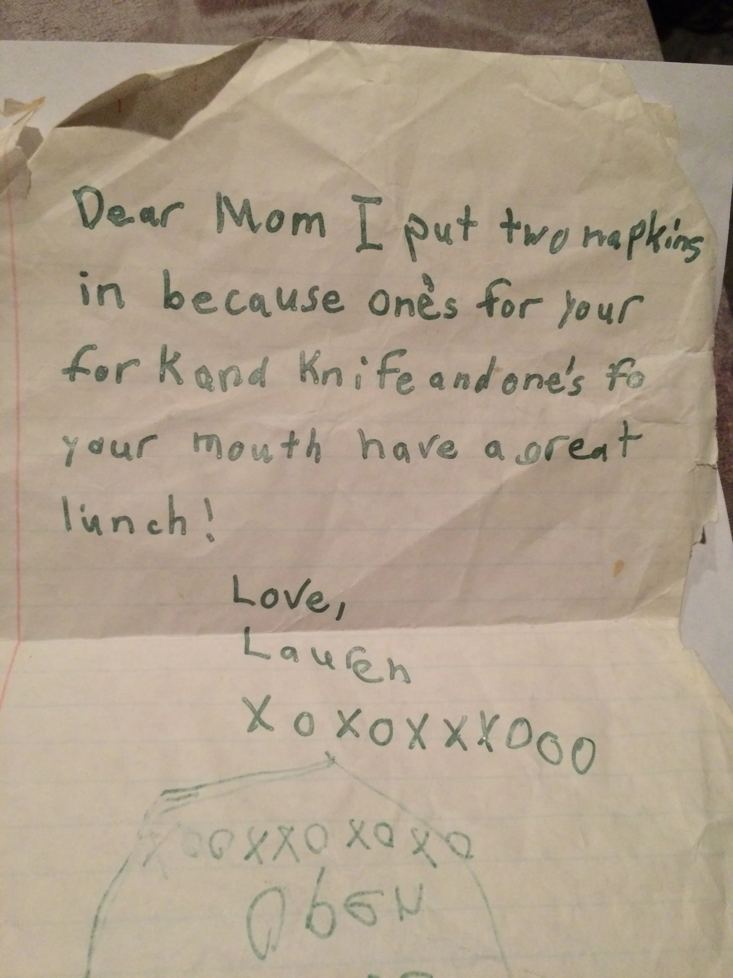 A handwritten note from a child to their mom on lined paper. The note explains that the child put two napkins in for the mom because one is for her fork and knife and one for her mouth. It includes a drawing and is signed with love, hugs, and kisses.