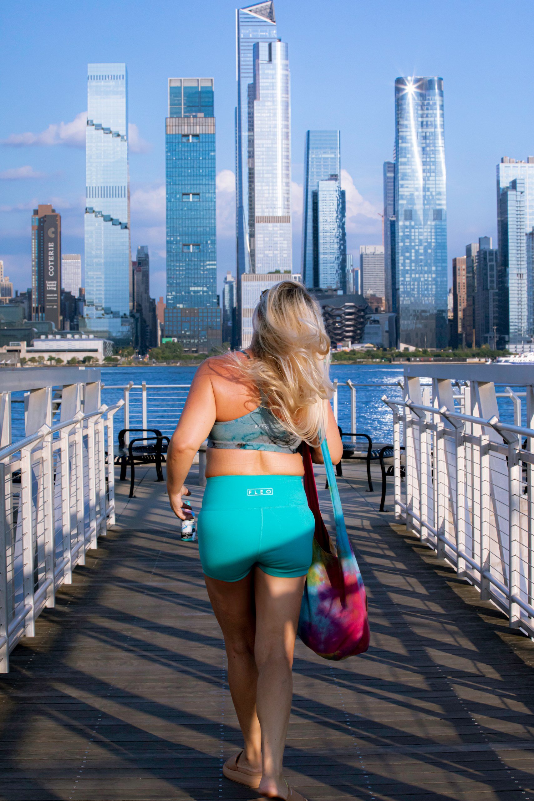 Woman in activewear walking on pier with city skyscrapers in background.