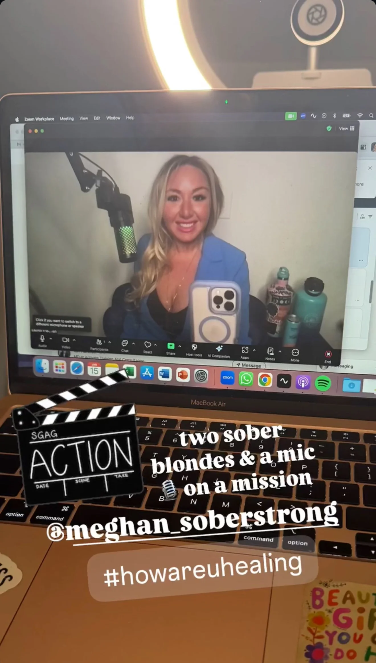 Zoom call screenshot with woman speaking into microphone, laptop keyboard with hashtag and username annotations, clapperboard graphic with text "two sober blondes & a mic on a mission @meghan_soberstrong #howareuhealing".