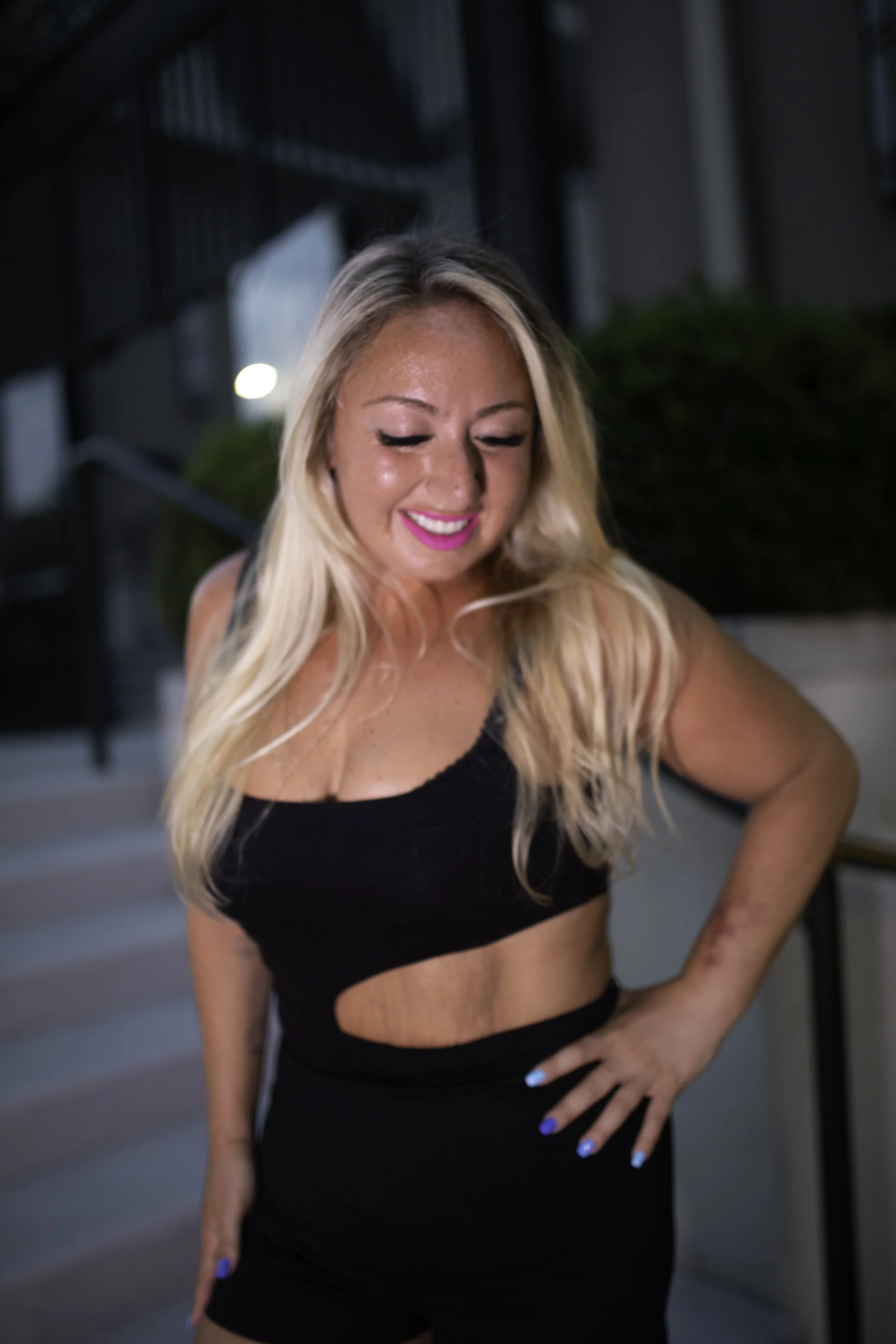 A woman with long blonde hair smiling, wearing a black outfit, standing outside.