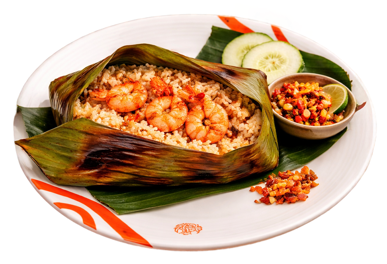 Plate of rice with shrimp wrapped in banana leaf, garnished with cucumber slices and lime wedge, accompanied by a bowl of spicy condiment and a side of lime slices and chopped ingredients.