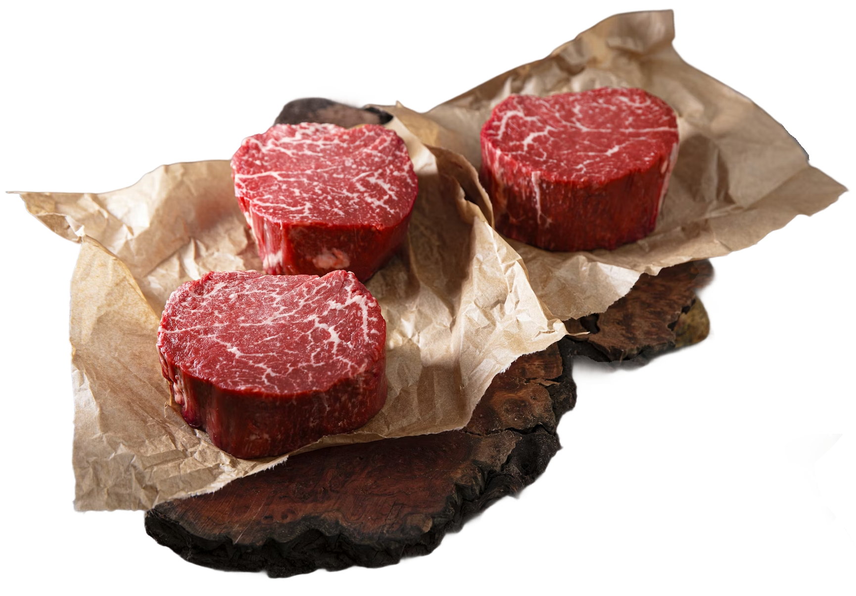 Three raw beef steaks with marbled fat on a rustic wooden surface, placed on crumpled parchment paper.