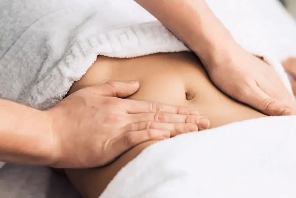 Close-up of a person receiving a massage on their stomach with hands gently pressing on their abdomen, with a white towel partially covering them.