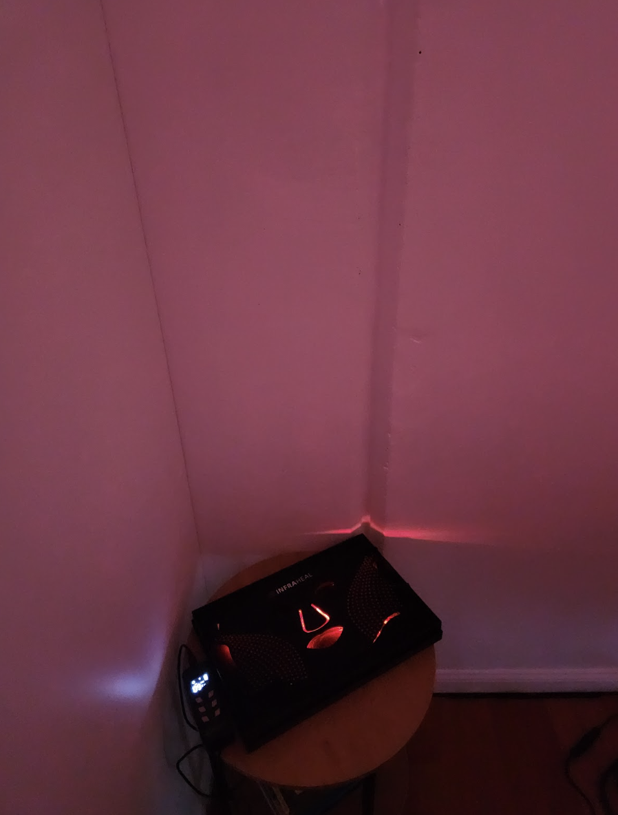 Infrared heater with a black casing and red lights, placed on a small round wooden table in a corner of a room with pink walls.