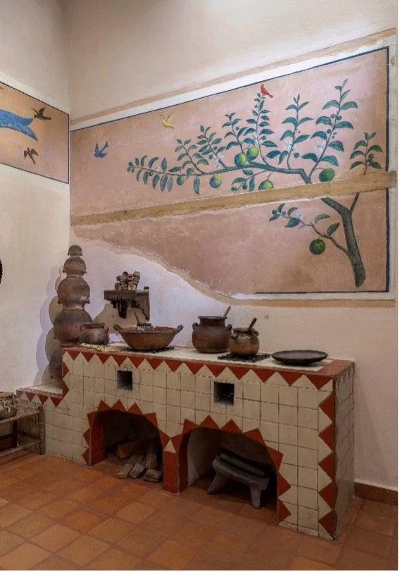 Decorative kitchen area with traditional clay pots and ceramics on a tiled countertop, and a painted mural of a lemon tree with birds on the wall.