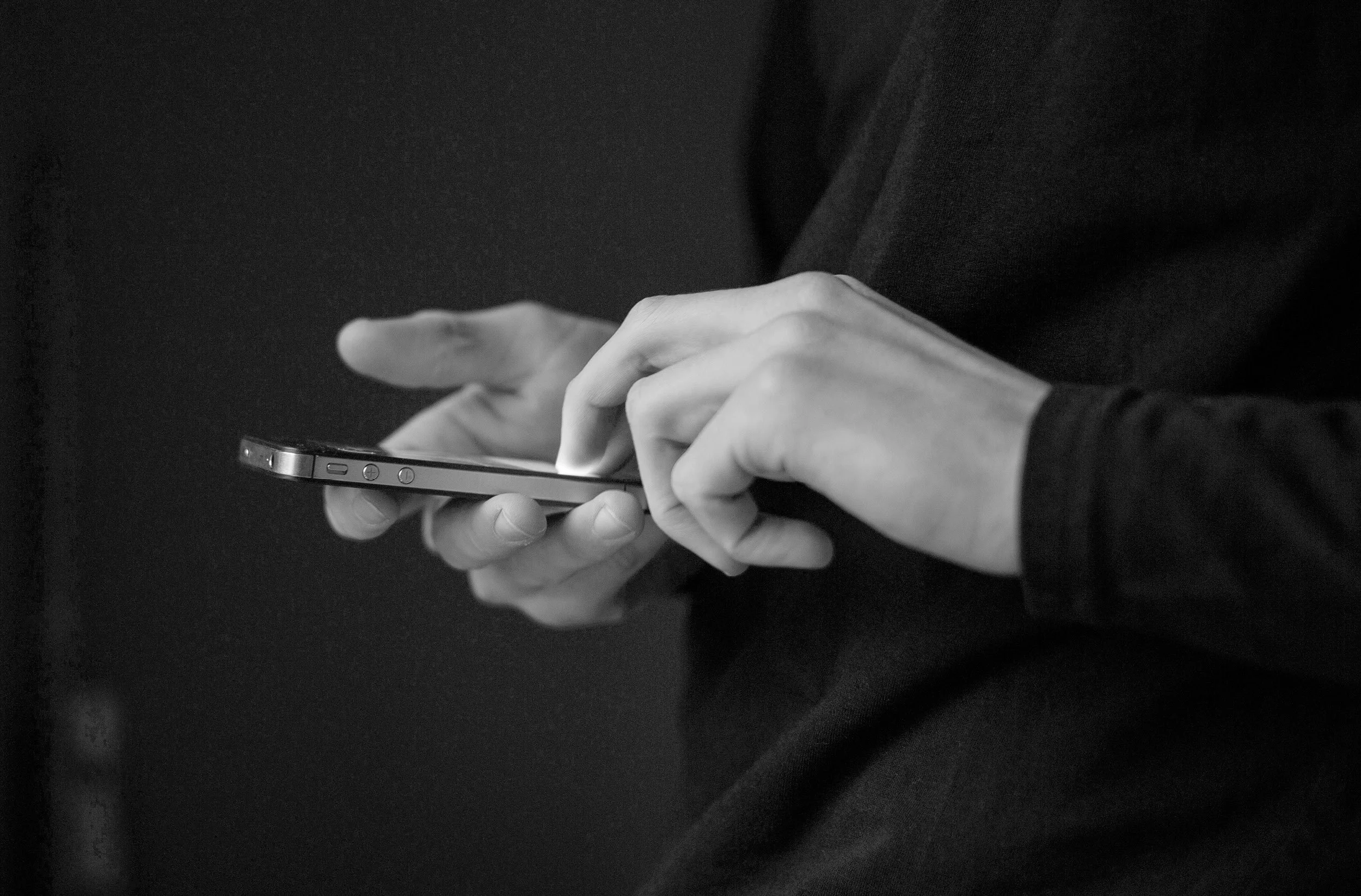 A person wearing black clothing holding and using a smartphone.