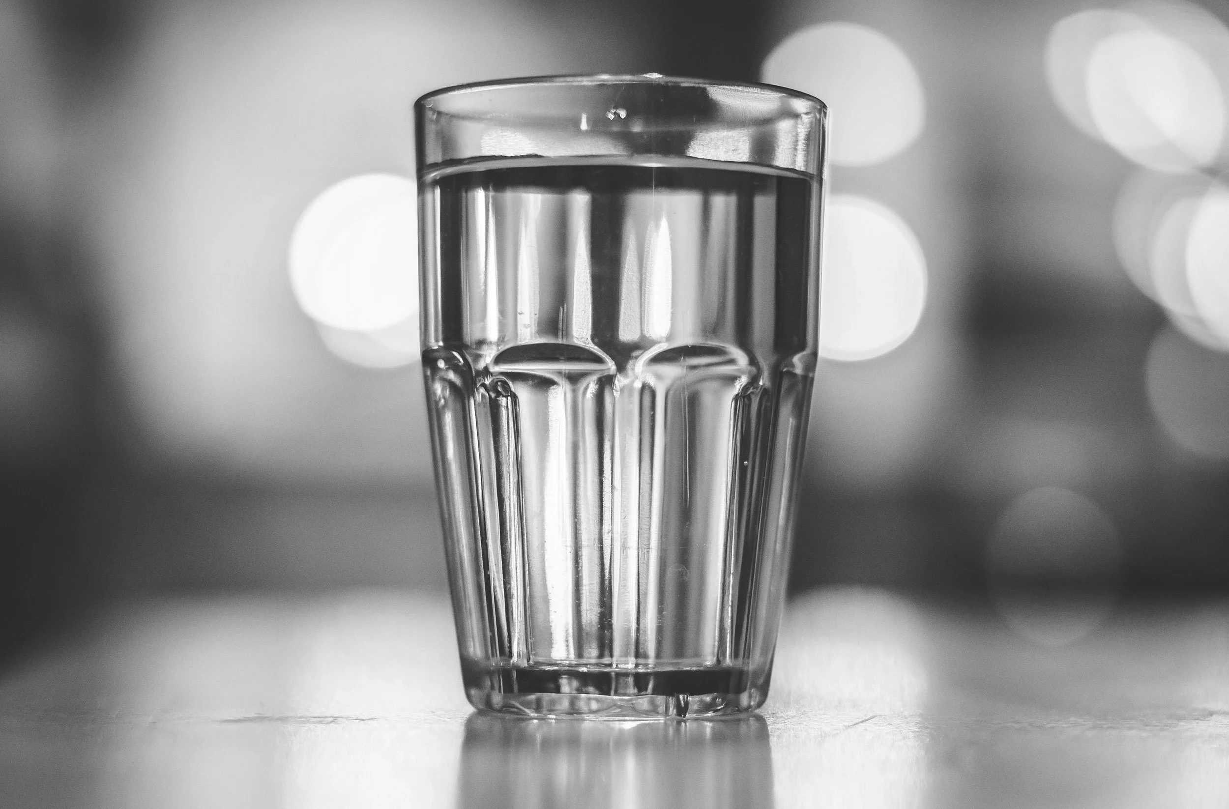 A clear glass of water placed on a surface with a blurred background of circular bokeh lights.