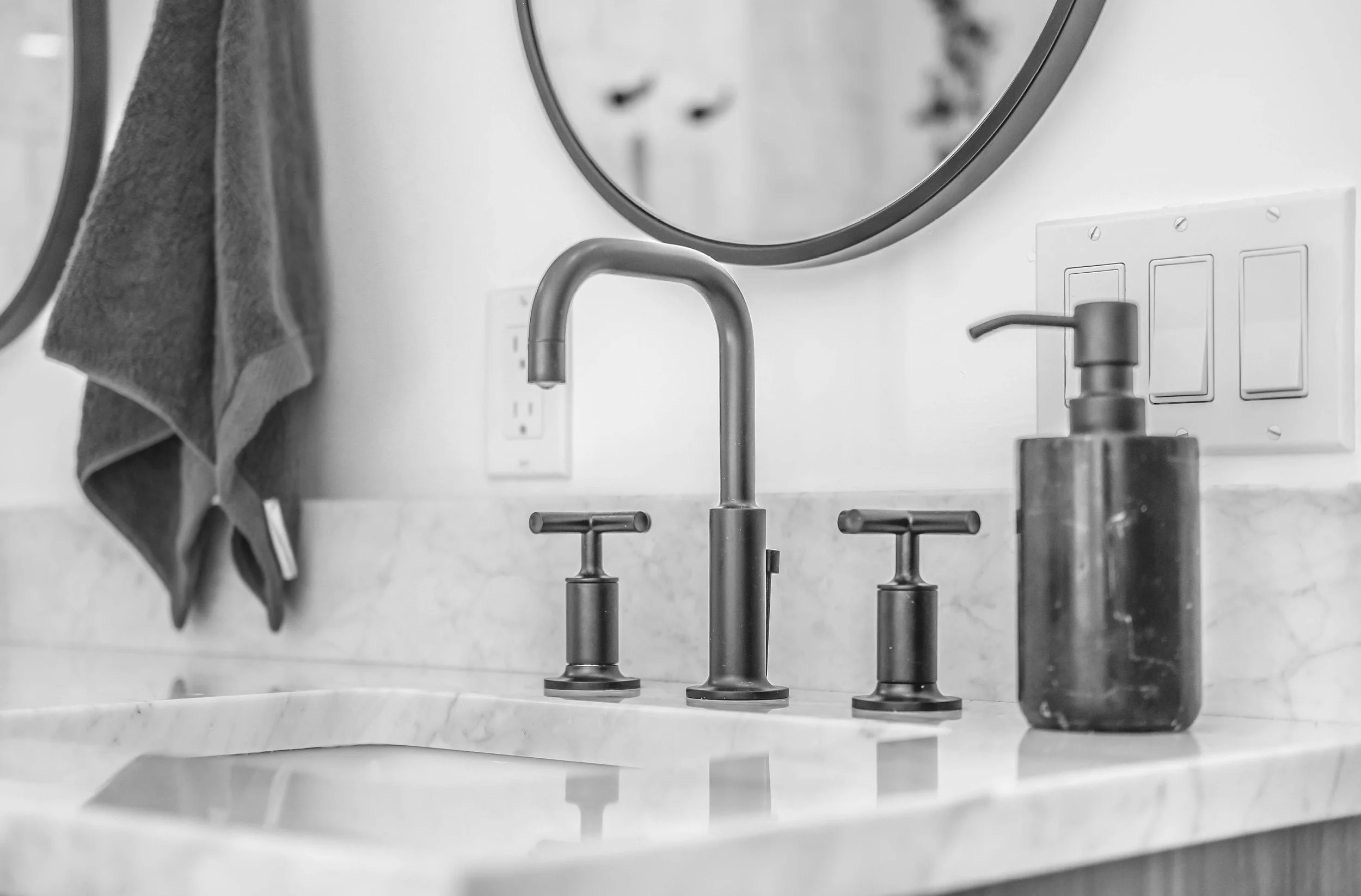 A bathroom sink with a modern faucet, soap dispenser, hanging towel, and a mirror above a marble countertop.
