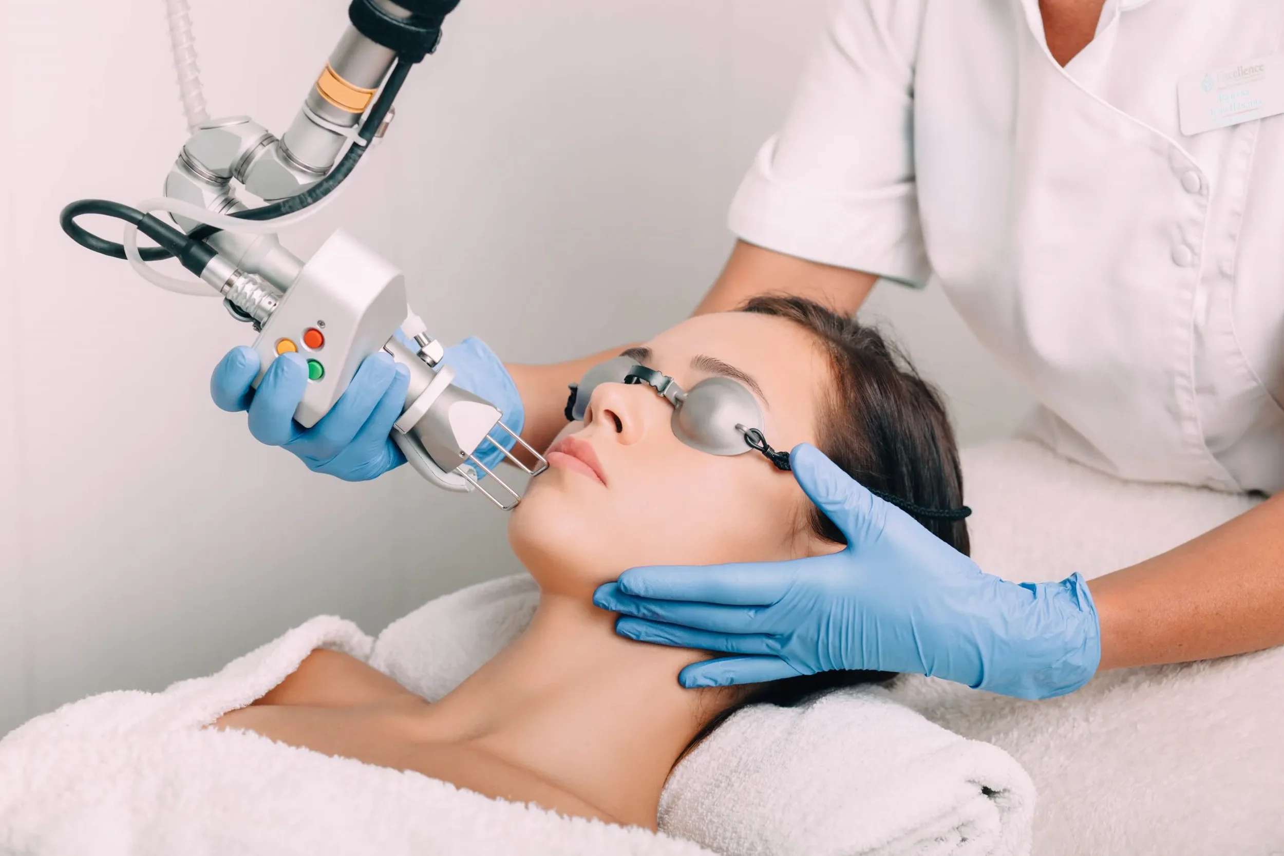 Medical professional performing a laser skin treatment on a woman lying down with eye protection, using a handheld device.