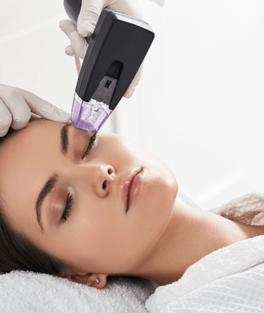 A woman receiving a facial treatment with a handheld device on her forehead in a spa or clinic setting.