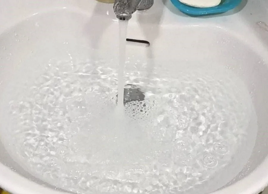 Running water from a faucet filling a white sink with bubbles and ripples.