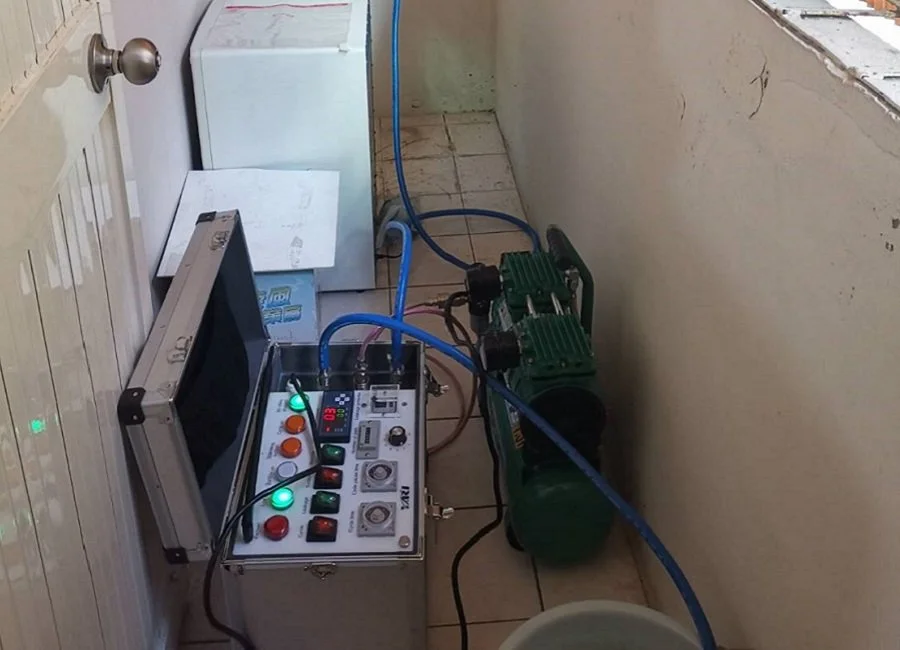 A soapy green water tank connected to electronic control panel with switches, buttons, and indicator lights, in a laundry room.